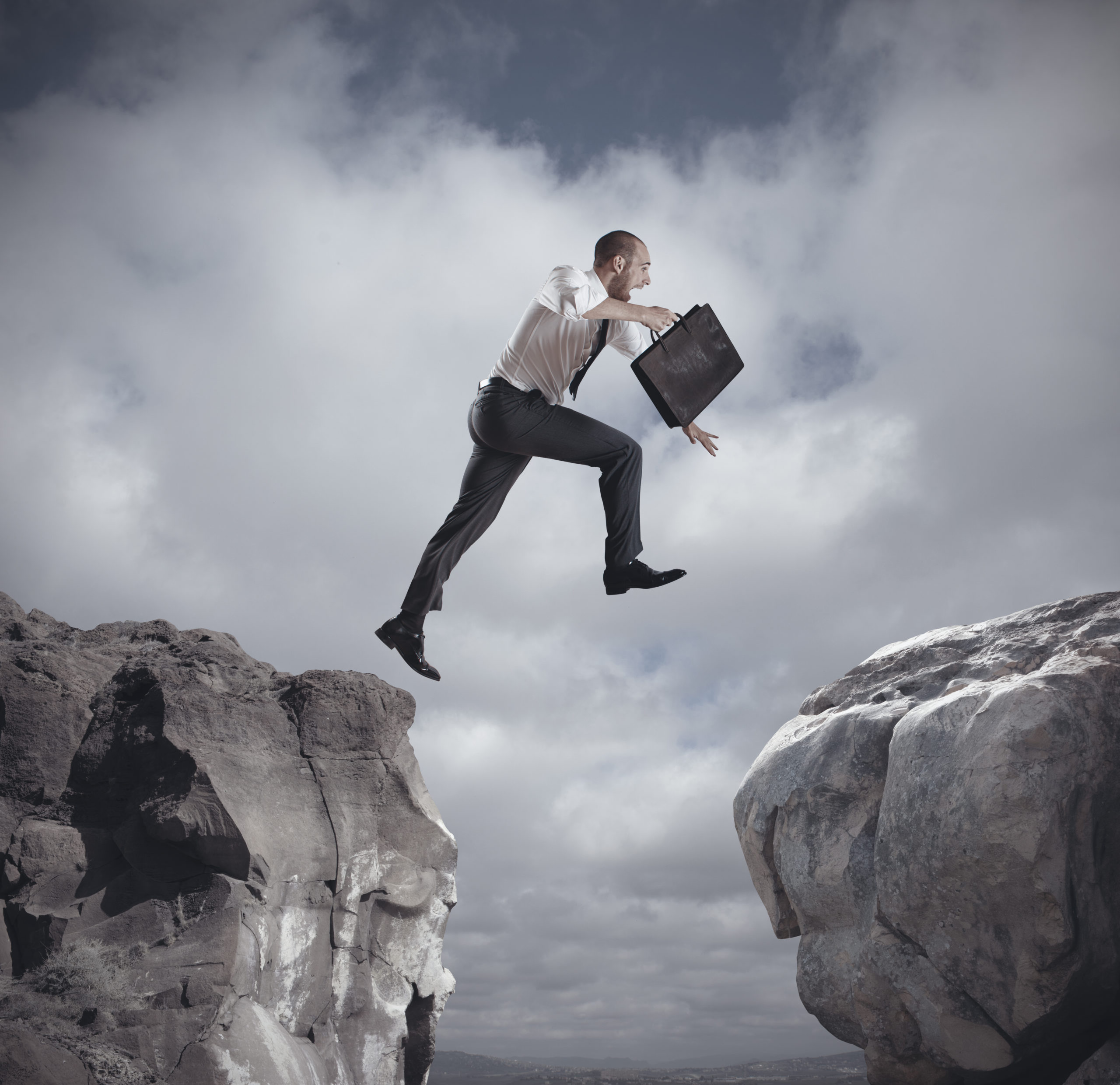 business man jumping over a cliff from one side to another while holding a brief case
